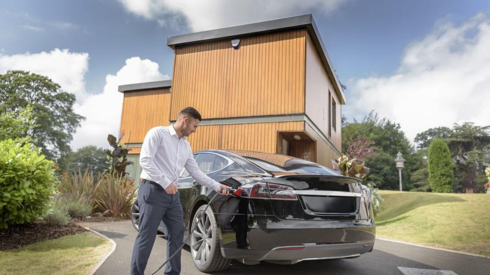 man charging electric car outside modern house