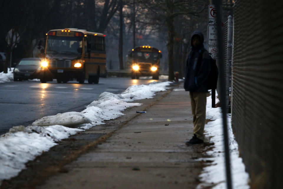 In this Feb. 5, 2019, photo, a student waits for a bus outside the abandoned John C. Clark Elementary and Middle School in Hartford, Conn. The school was closed in 2015 after toxic PCBs were found during a renovation. Many students in the neighborhood now must travel long distances to get to other schools. (AP Photo/Martha Irvine)