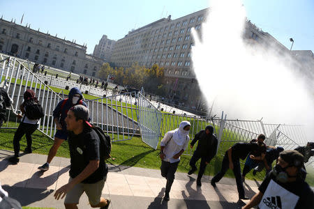 Demonstrators run away from a jet of water released by a riot police vehicle during a protest calling for changes in the education system in Santiago, Chile April 11, 2017. REUTERS/Ivan Alvarado