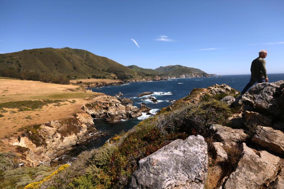 A man stands on a rock outcropping overlooking the ocean.