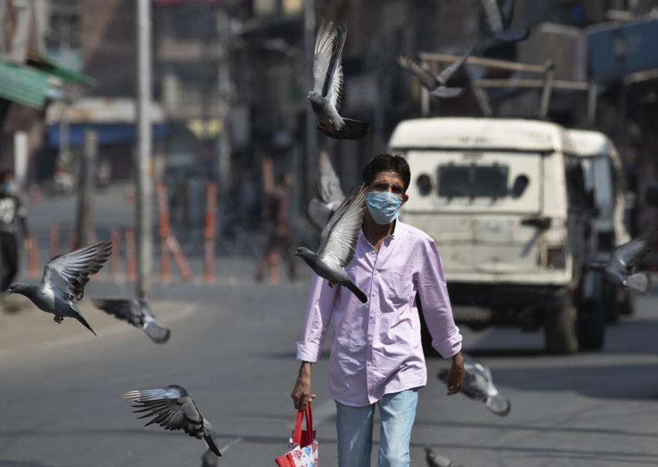 Pigeons fly as a man wearing a mask walks past in Srinagar, Indian controlled Kashmir, Monday, July 13, 2020. Authorities reimposed lockdown on Monday in parts of Indian-controlled Kashmir, including the region's main city, following surge in coronavirus cases. (AP Photo/Mukhtar Khan)