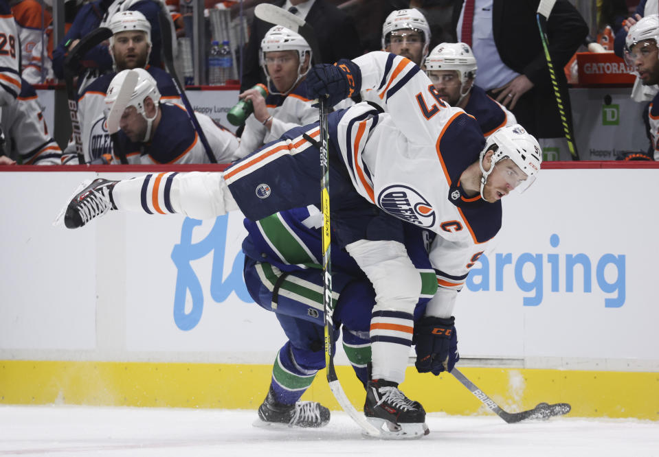 Edmonton Oilers' Connor McDavid, front, is checked by Vancouver Canucks' Tyler Motte during the second period of an NHL hockey game, Tuesday, Jan. 25, 2022 in Vancouver, British Columbia. (Darryl Dyck/The Canadian Press via AP)