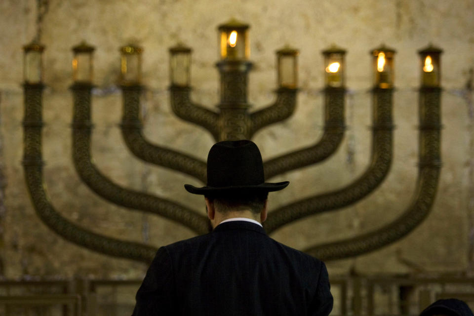 FILE - An Ultra-Orthodox Jewish man stands in front of a menorah on the third eve of Hanukkah, at the Western Wall, Judaism's holiest site in Jerusalem's old city, Sunday, Dec. 13, 2009. On eight consecutive nightfalls, Jews gather with family and friends to light one additional candle in the menorah candelabra. They do so to commemorate the rededication of the Temple in Jerusalem in the 2nd century BC, after a small group of Jewish fighters liberated it from occupying foreign forces. (AP Photo/Sebastian Scheiner, File)