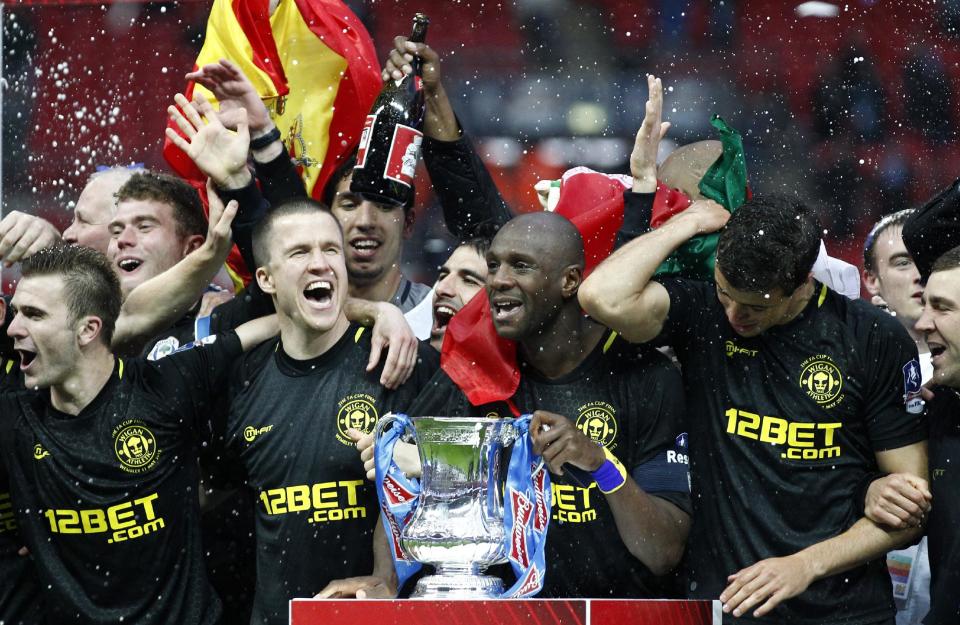 FILE - In this Saturday, May 11, 2013 file photo, Wigan Athletic players including their captain Emmerson Boyce, centre right, celebrate after their 1-0 win over Manchester City in their English FA Cup final soccer match at Wembley Stadium, London. Wigan Athletic hadn’t won a piece of major silverware in its 81-year history until last May, when it pulled off one of the great FA Cup upsets by beating big-spending Manchester City in the final. Now, despite dropping out of the Premier League at the end of last season, it is on course to retain the famous trophy against all the odds. (AP Photo/Jon Super, File)