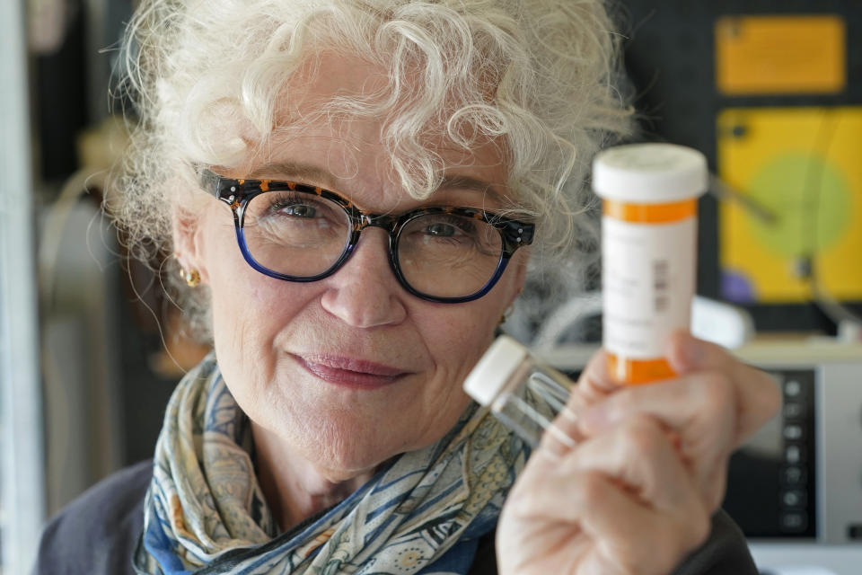 Mary Beth Orr poses for a photo in her home, Tuesday, Aug. 23, 2022 in Burien, Wash., south of Seattle, while holding medicine bottles used to give her doses of psilocybin, the compound in psychedelic mushrooms, as part of a study to try and help heavy drinkers cut back or quit entirely. Orr used to have five or six drinks every evening and more on weekends before she enrolled in the study in 2018. She stopped drinking entirely for two years, and now has an occasional glass of wine, and credits psilocybin for her progress. (AP Photo/Ted S. Warren)