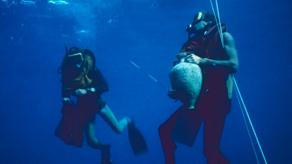  Two scuba divers holding artifacts while underwater. 