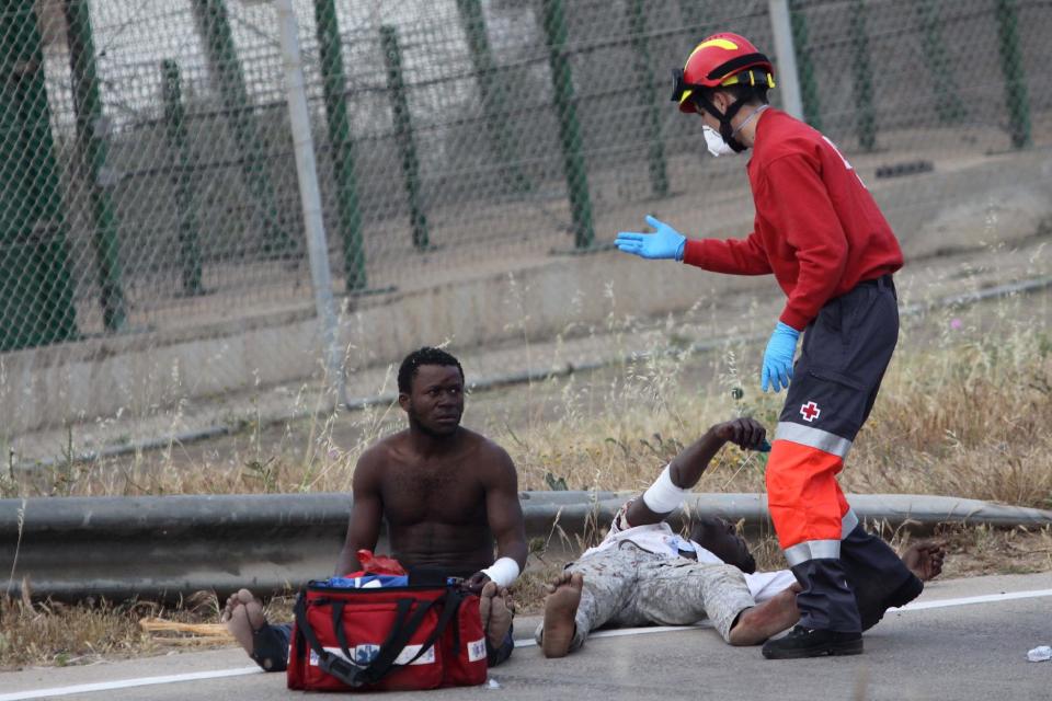 Sub-Saharan migrants sit on the Spanish soil as a Red Cross worker is on-hand to offer humanitarian assistance, next to a metallic fence that divides Morocco and the Spanish enclave of Melilla, Thursday, May 1, 2014. Spain says around 700 African migrants have rushed its barbed wire border fences in the North African enclave of Melilla, and although police repelled most, 140 managed to enter Spanish territory. The migrants charged the fences in two waves, with 500 arriving in the early hours and another 200 later Thursday morning. Spain and Morocco stepped up border vigilance in Feb. when 15 migrants drowned trying to enter Spain's other north African coastal enclave, Ceuta. (AP Photo/Fernando Garcia)