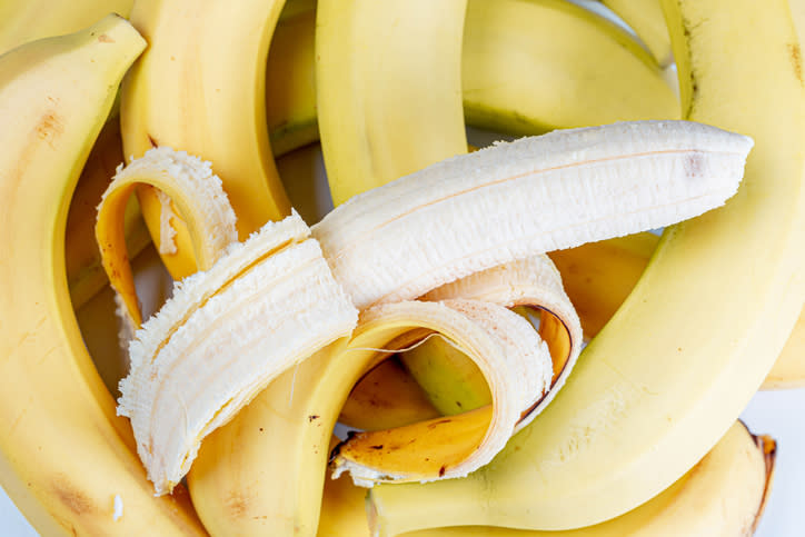 A bunch of bananas with one partially peeled banana in the center