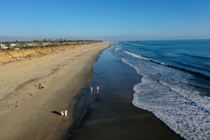 Huntington Beach, CA - October 05: An aerial view of environmental oil spill cleanup crews picking up oil chucks off the beach from a major oil spill at Huntington Dog Beach in Huntington Beach Tuesday, Oct. 5, 2021. Environmental cleanup crews are spreading out across Huntington Beach and Newport Beach to cleanup the damage from a major oil spill off the Orange County coast that left crude spoiling beaches, killing fish and birds and threatening local wetlands. The oil slick is believed to have originated from a pipeline leak, pouring 126,000 gallons into the coastal waters and seeping into the Talbert Marsh as lifeguards deployed floating barriers known as booms to try to stop further incursion, said Jennifer Carey, Huntington Beach city spokesperson. At sunrise Sunday, oil was on the sand in some parts of Huntington Beach with slicks visible in the ocean as well. "We classify this as a major spill, and it is a high priority to us to mitigate any environmental concerns," Carey said. "It's all hands on deck." (Allen J. Schaben / Los Angeles Times)