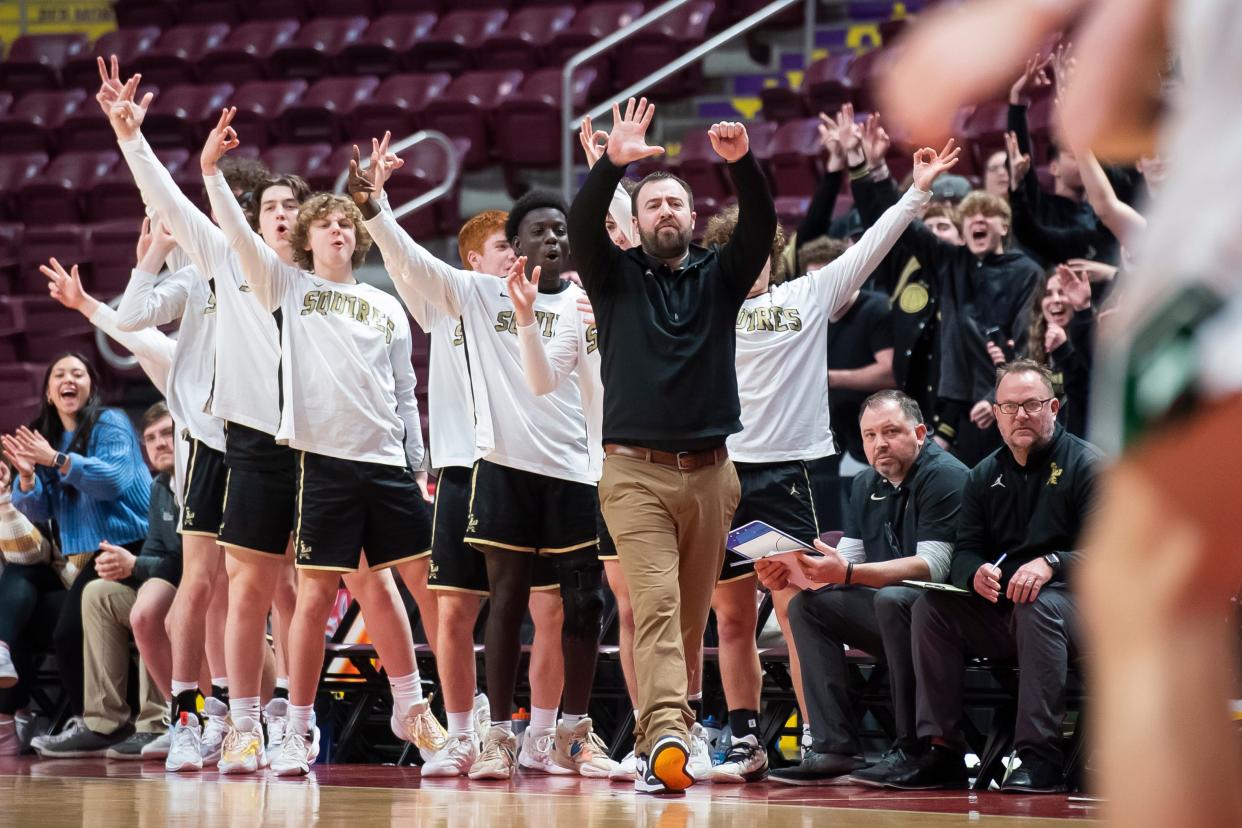 Delone Catholic head coach Brandon Staub and the Squires bench react after Gage Zimmerman nails a 3-pointer to open the game against Trinity in the District 3 Class 3A boys' basketball championship at the Giant Center on Feb. 28, 2023, in Derry Township.