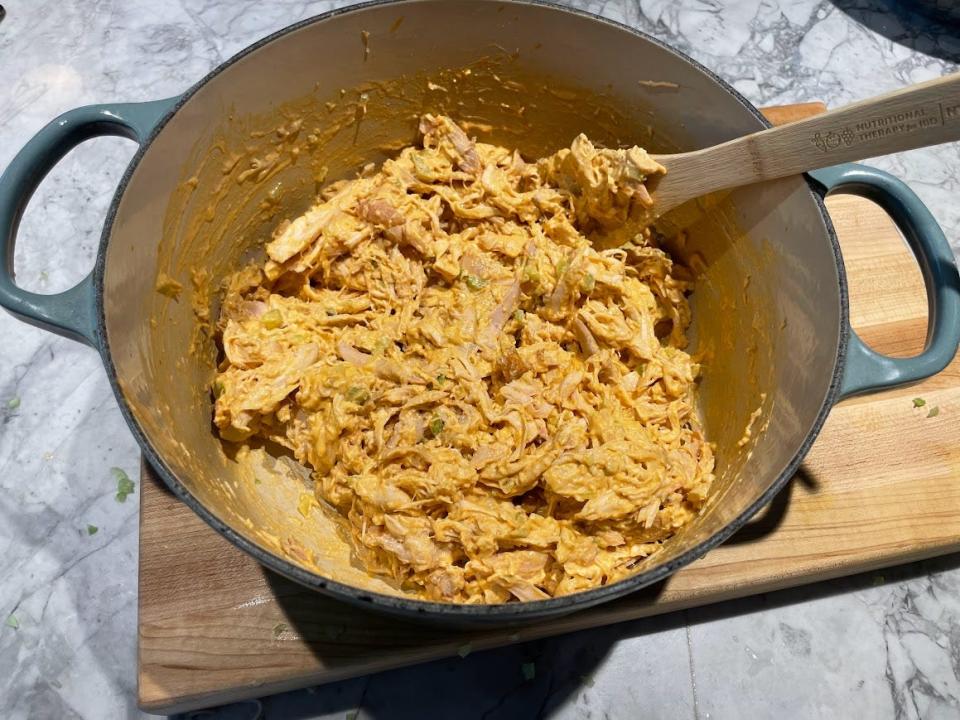 A Dutch oven filled with Buffalo-chicken dip with visible pieces of celery and chicken. A wooden spoon is placed in the dip