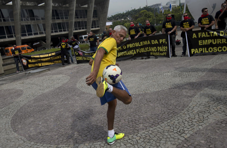 A Brazil soccer fan kicks a ball where federal police protest for better labor conditions outside the venue where Brazil's coach is announcing his squad for the upcoming international soccer tournament in Rio de Janeiro, Brazil, Wednesday, May 7, 2014. The team will mix talented young stars such as Neymar and Oscar with more experienced players such as Dani Alves, David Luiz, Thiago Silva and Hulk. Past stars such as Ronaldinho, Kaka and Robinho were left off the squad as expected. Federal police are threatening to go on strike during the international soccer tournament if their demands are not met. (AP Photo/Silvia Izquierdo)