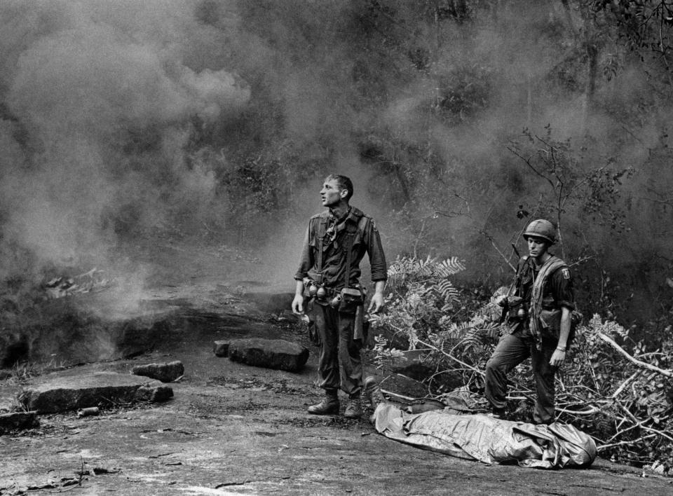 Spc. Ruediger Richter, 4th Battalion, 173rd Airborne Brigade, gazes into the smoke of a directional grenade for the arrival of an evacuation helicopter in a jungle clearing on Long Khanh Province, South Vietnam, October 1966. Sgt. Daniel E. Spencer of Bend, stands by the poncho wrapped body of a dead comrade. (AP Photo/Pfc. L. Paul Epley)