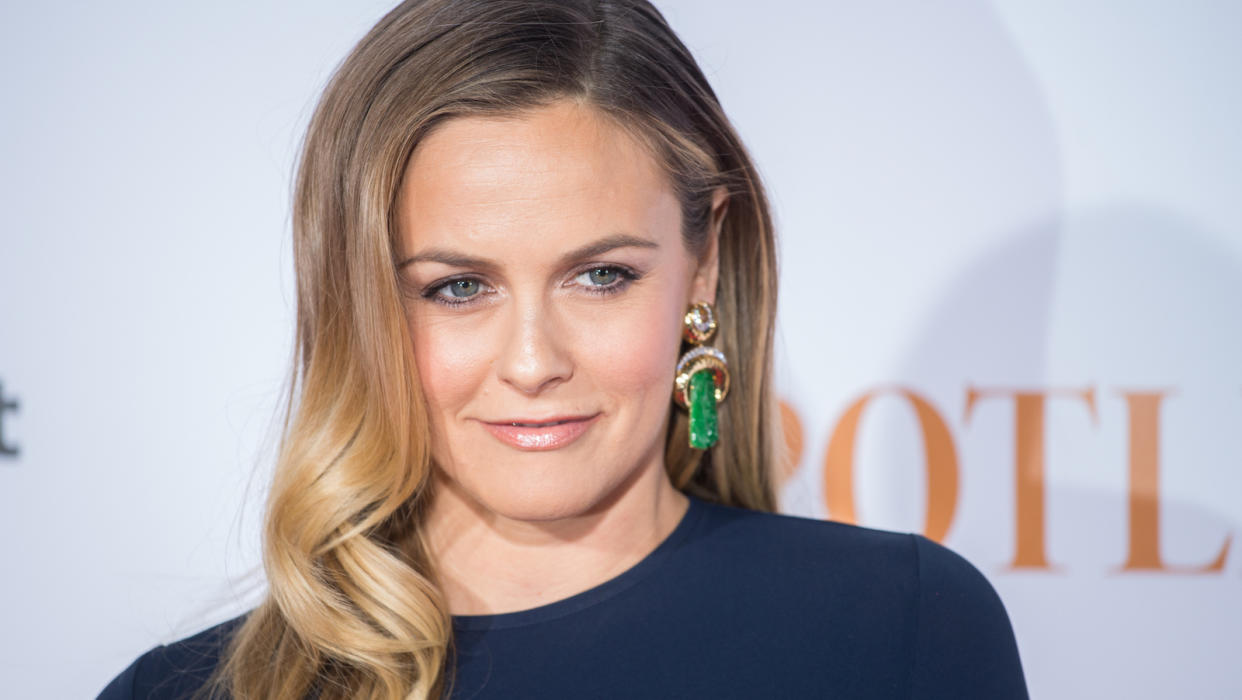  Alicia silverstone in a blue top and green earrings at a press event . 