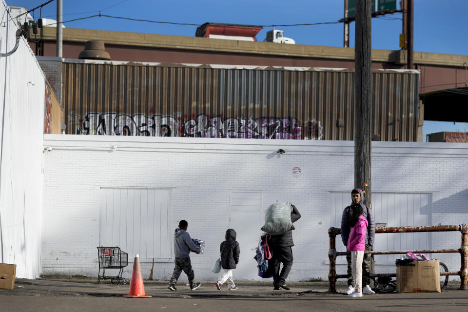 Immigrants stand outside and return to a shelter in the Pilsen neighborhood of Chicago, Tuesday, Dec. 19, 2023. The death of a 5-year-old migrant boy and reported illnesses in other children living at the shelter has raised concerns about the living conditions and medical care provided for asylum-seekers arriving in Chicago. Four more people living in the same shelter — mostly children — were hospitalized with fevers this week. (AP Photo/Charles Rex Arbogast)