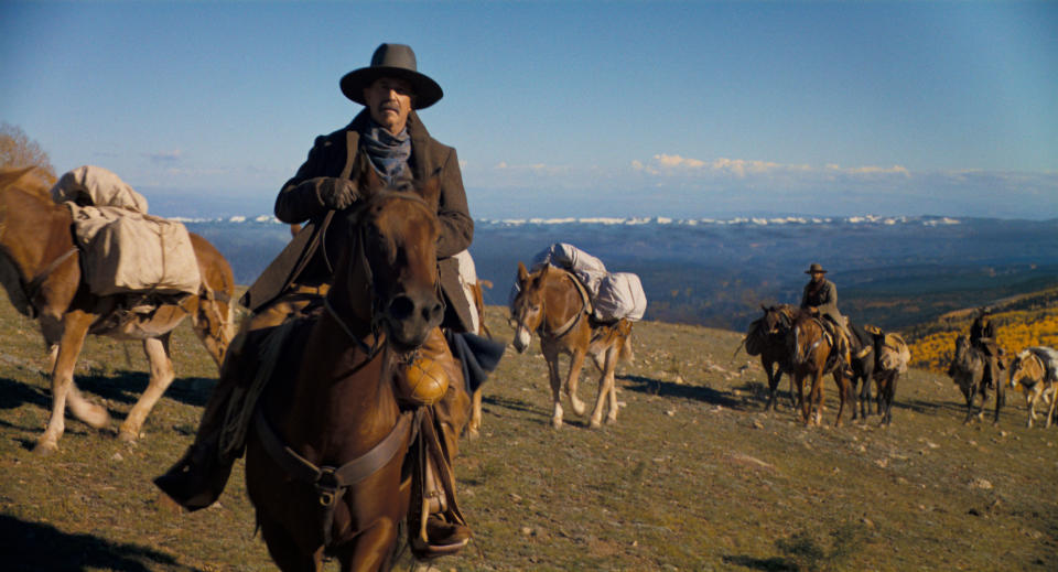 Cowboys on horseback leading a pack train across a mountainous landscape