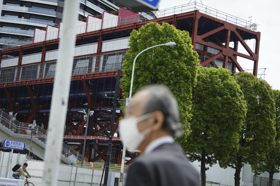 FILE - In this April 6, 2021, file photo, aman wearing a protective mask to help curb the spread of the coronavirus walks across a street as a massive steel structure in front of Japan National Stadium, where opening ceremony and many other events are planned for postponed Tokyo 2020 Olympics, in Tokyo. Public sentiment in Japan has been generally opposed to holding the Tokyo Olympics and Paralympics. This is partly based of fears the coronavirus will spike as almost 100,000 people — athletes and others — enter for both events. (AP Photo/Eugene Hoshiko, File)