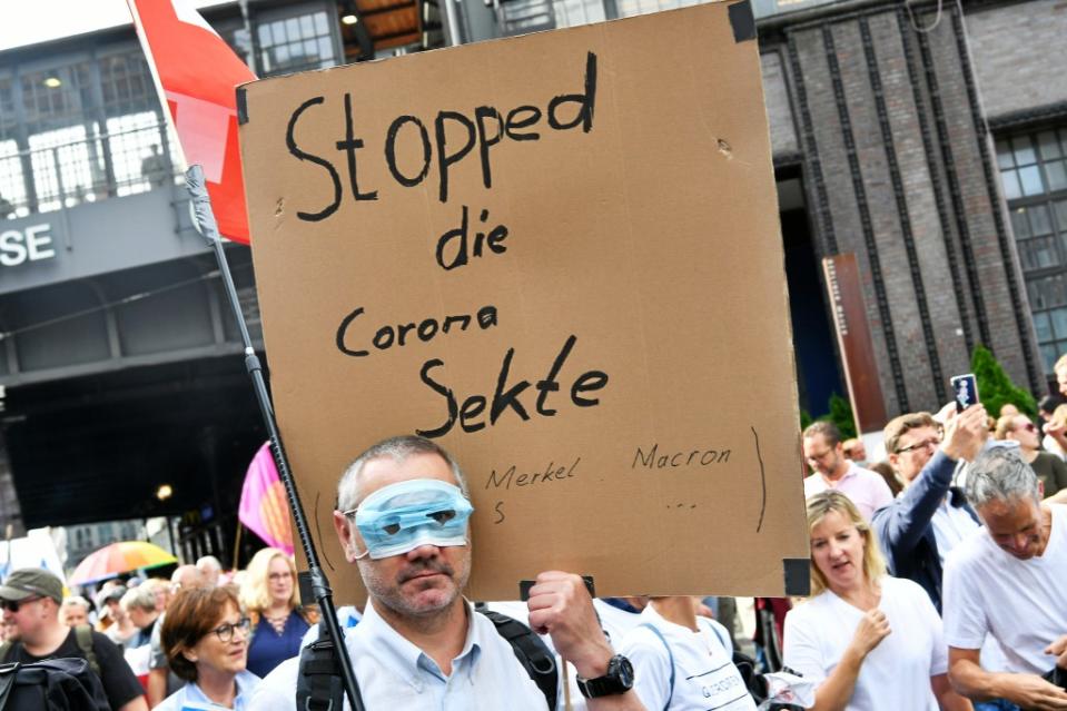 Ein Teilnehmer mit einem Mundschutz über den Augen und dem Schild "Stopped die Corona Sekte" steht in der Friedrichstraße bei einer Demonstration gegen die Corona-Maßnahmen.<span class="copyright">Paul Zinken / dpa</span>