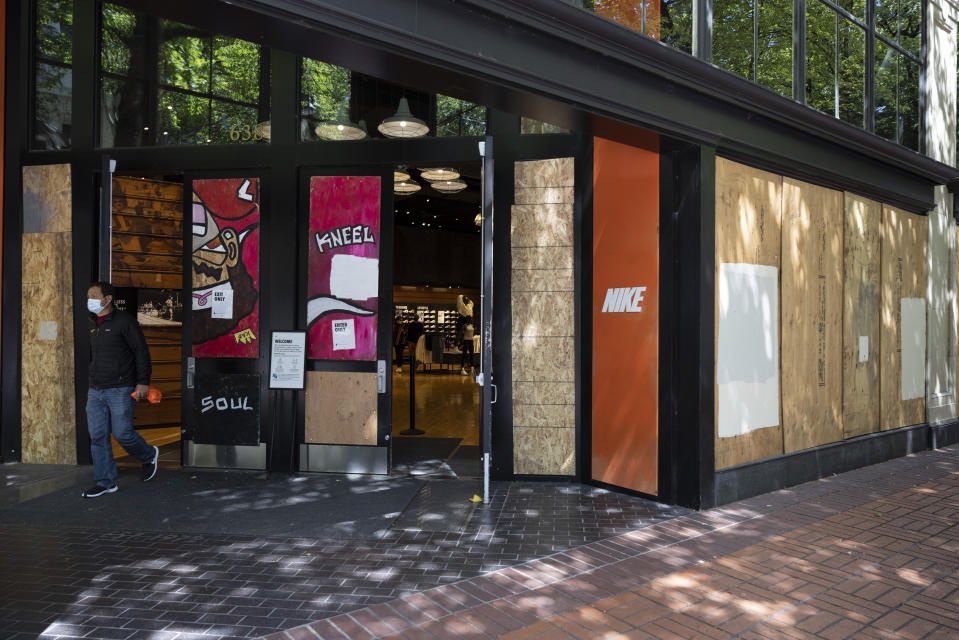 A man walks out of the Nike store which is protected by wooden panels to prevent windows being broken by on-going protests in downtown Portland, Ore., on Saturday, June 5, 2021. City officials insist Portland is resilient as they launch a revitalization plan — in the form of citywide cleanups of protest damage, aggressive encampment removals, increased homeless services and police reform — to repair its reputation. (AP Photo/Paula Bronstein)
