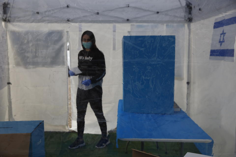 A volunteer wearing a face mask is seen through a sheet of plastic demonstrating how Israeli voters who are quarantined due to new virus will vote, in a sterile tent designated as a polling station, in Tel Aviv, Israel, Sunday, March 1, 2020. Israel heads into its third election in less than a year on Monday, March 2nd. (AP Photo/Ariel Schalit)