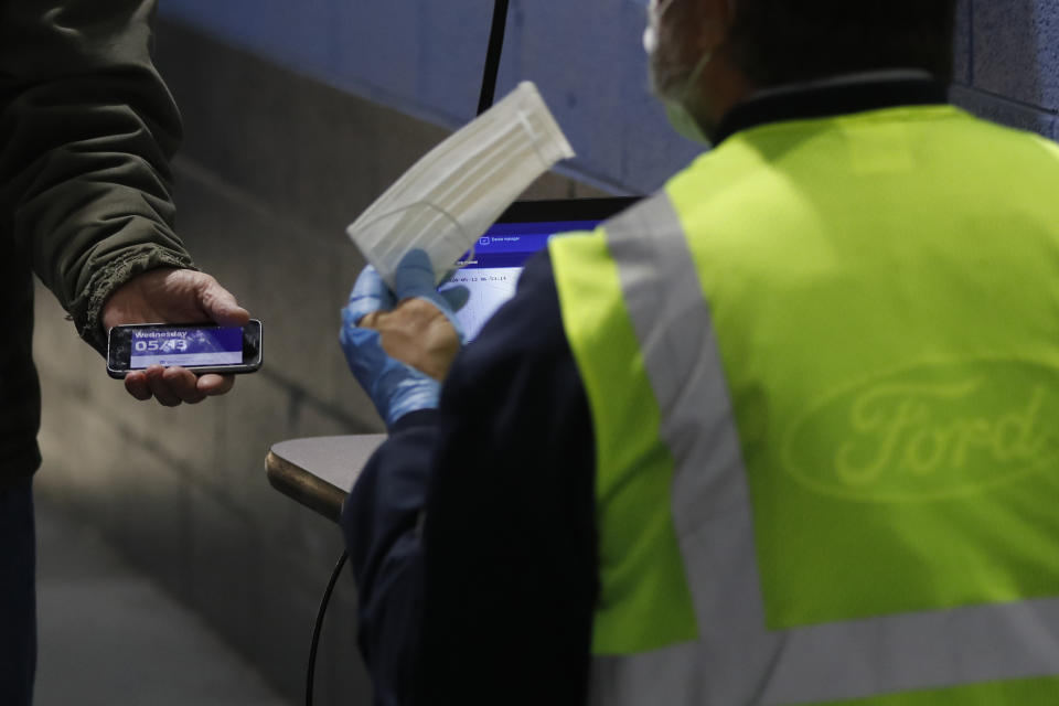 A Ford employee, left, shows his COVID-19 daily survey pass and is given a face mask as he enters the Ford Rawsonville plant, Wednesday, May 13, 2020 in Ypsilanti Township, Mich. The plant was converted into a ventilator factory, as hospitals battling the coronavirus report shortages of the life-saving devices. The company has promised to deliver 50,000 by July 4. Ford and other automakers are preparing for the reopening of their plants next week. Factories must adopt measures to protect their workers, including daily entry screening and, once they are available, the use of no-touch thermometers. Those measures already are in effect at Rawsonville. (AP Photo/Carlos Osorio)