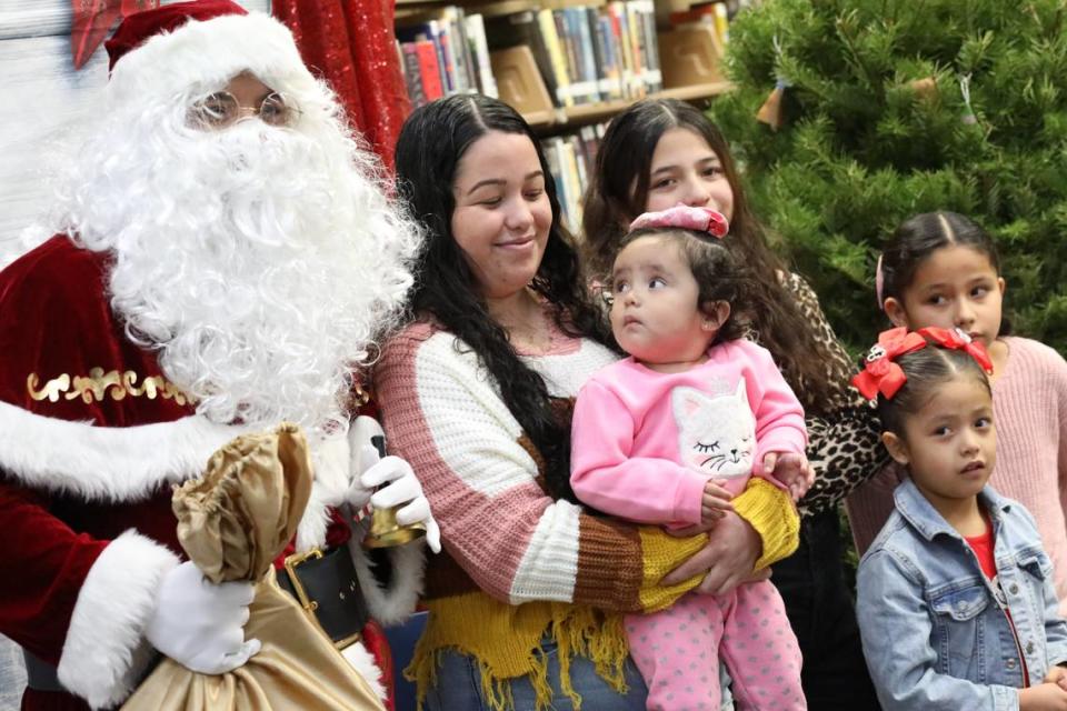 Isela Molina sonríe mientras su hija Yetzali Ayala (centro), de 1 año de edad, mira de cerca a Santa Clos durante el evento de Navidad de la Familia Migrante 2023 que tuvo lugar en la biblioteca de la Firebaugh High School el 13 de diciembre.