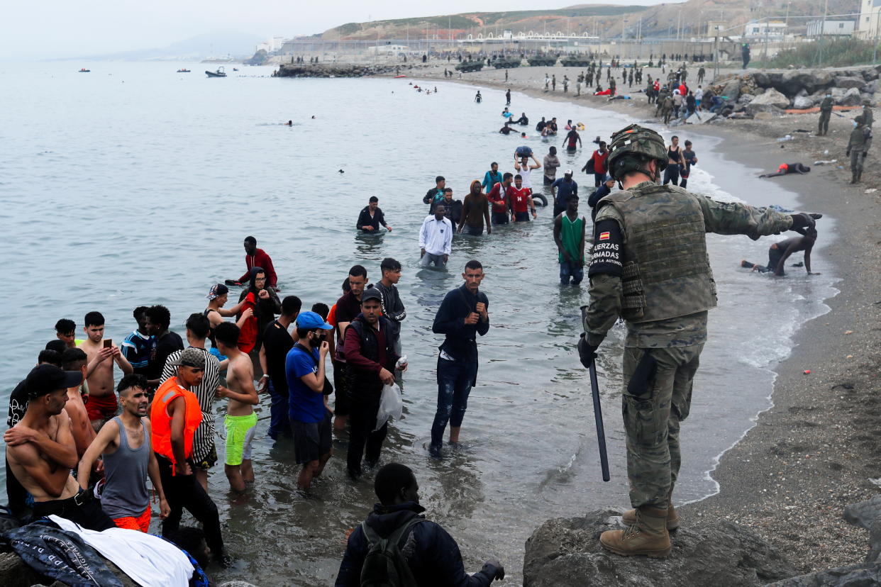 A Spanish legionnaire indicates the direction to follow to Moroccan citizens on El Tarajal beach, as they get out of the water on the Spanish side of the fence between the Spanish-Moroccan border, after thousands of Moroccans swam across this border on Monday, in Ceuta, Spain, May 18, 2021. REUTERS/Jon Nazca