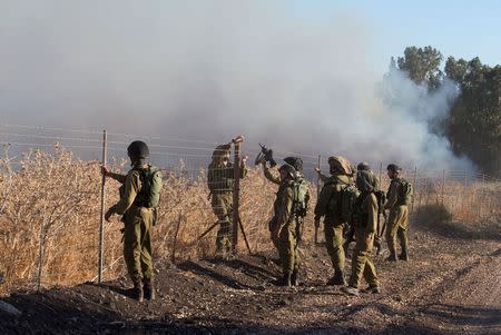 Israeli soldiers stand next to smoke from a fire caused by a rocket attack in northern Israel, near the Lebanese border, August 20, 2015. REUTERS/JINIPIX