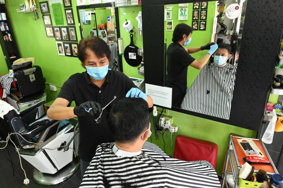 A barber wearing a face mask as a prevention measure against the spread of the COVID-19 coronavirus attends to a customer at a hair salon, after they reopened as restrictions to contain the outbreak were relaxed, in Singapore on May 12, 2020. (Photo by ROSLAN RAHMAN / AFP) (Photo by ROSLAN RAHMAN/AFP via Getty Images)