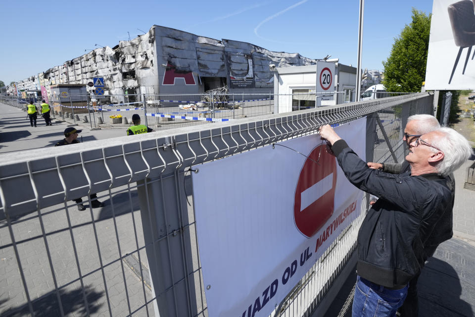 Authorities putting up a "No Entry" sign on a temporary fence put up to block access to a burnt-down shopping center in Warsaw, Poland, on Wednesday, May 15, 2024. A weekend fire at the Marywilska 44 shopping center dealt tragedy to many members of Poland's Vietnamese community. People lost entire livelihoods and say they don't know how they will manage to make a living. 2024. (AP Photo/Czarek Sokolowski)