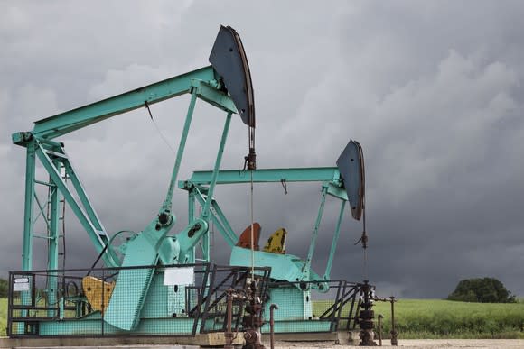 Two green oil wells sitting under a dark stormy grey sky.