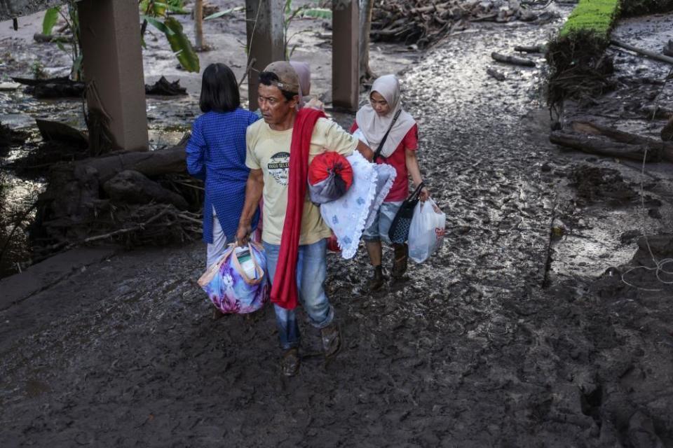 Villagers carry their belongings as they walk through mud following a flash flood in Tanah Datar