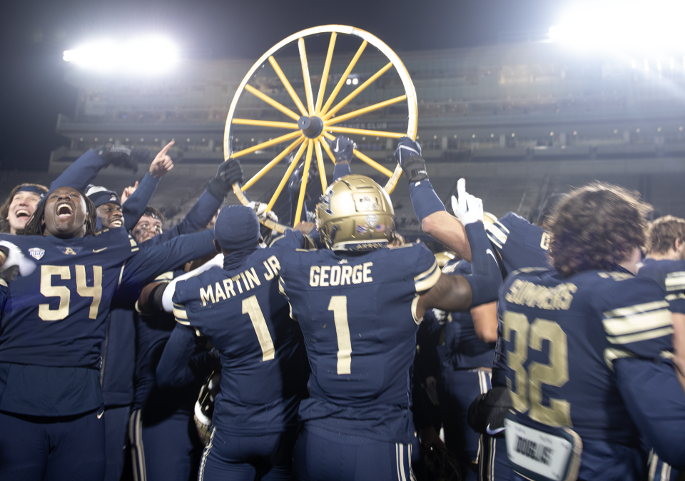 University of Akron players hold up the Wagon Wheel after defeating Kent State on Wednesday night in Akron.