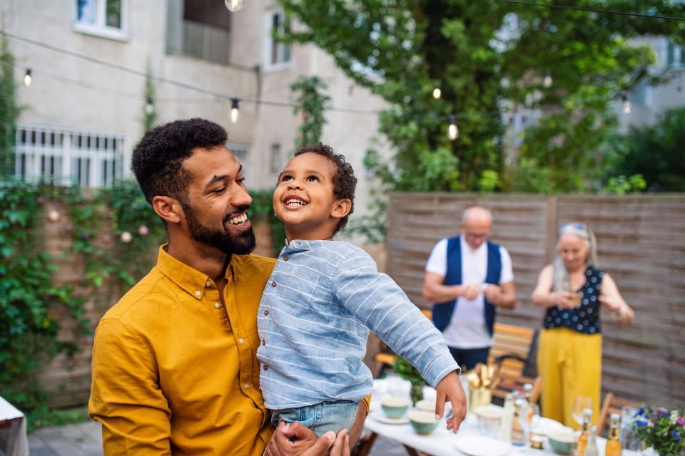 Happy young father holding his little son laughing and having fun during family dinner outdoors in back yard.