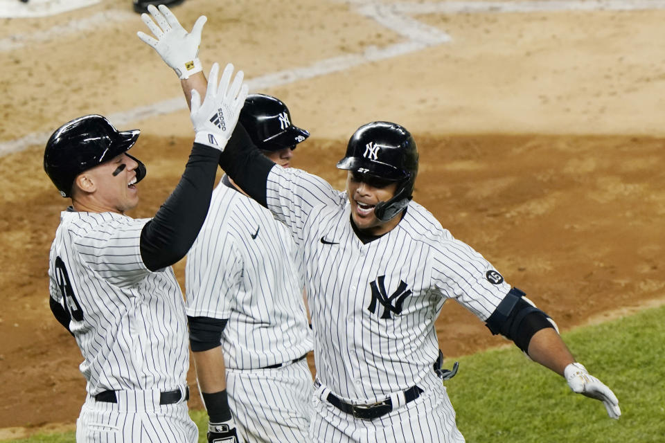 New York Yankees' Aaron Judge, left, celebrates with designated hitter Giancarlo Stanton after also scoring on Stanton's fifth-inning grand slam in a baseball game against the Baltimore Orioles, Monday, April 5, 2021, at Yankee Stadium in New York. Yankees' DJ LeMahieu passes behind the pair. (AP Photo/Kathy Willens)