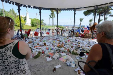 People stop near flowers left in tribute at a makeshift memorial to the victims of the Bastille Day truck attack along the Promenade des Anglais in Nice, France, July 21, 2016. REUTERS/Jean-Pierre Amet