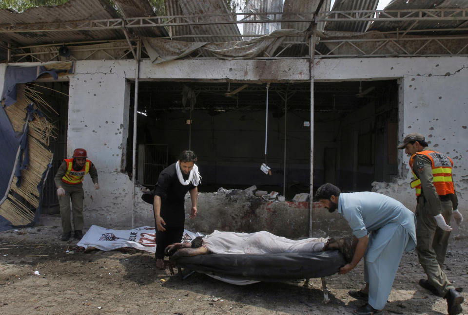 Pakistani volunteers and rescue workers remove a lifeless body from the site after a bomb explosion in Peshawar, Pakistan, Sunday, May 11, 2014. A police official in Pakistan says a bomb blast targeting refugees registering with the government has killed several people in northwestern city of Peshawar. Faisal Mukhtar says the bombing Sunday on a soccer field also wounded many people. He says it happened as officials registered refugees from the nearby Khyber tribal region. (AP Photo/Mohammad Sajjad)