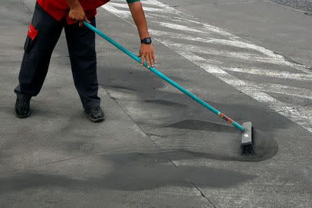 An employee sweeps the entrance of a gas station covered with ash after Guatemala's Fuego volcano erupted violently, in Guatemala City, Guatemala June 3, 2018. REUTERS/ Luis Echeverria