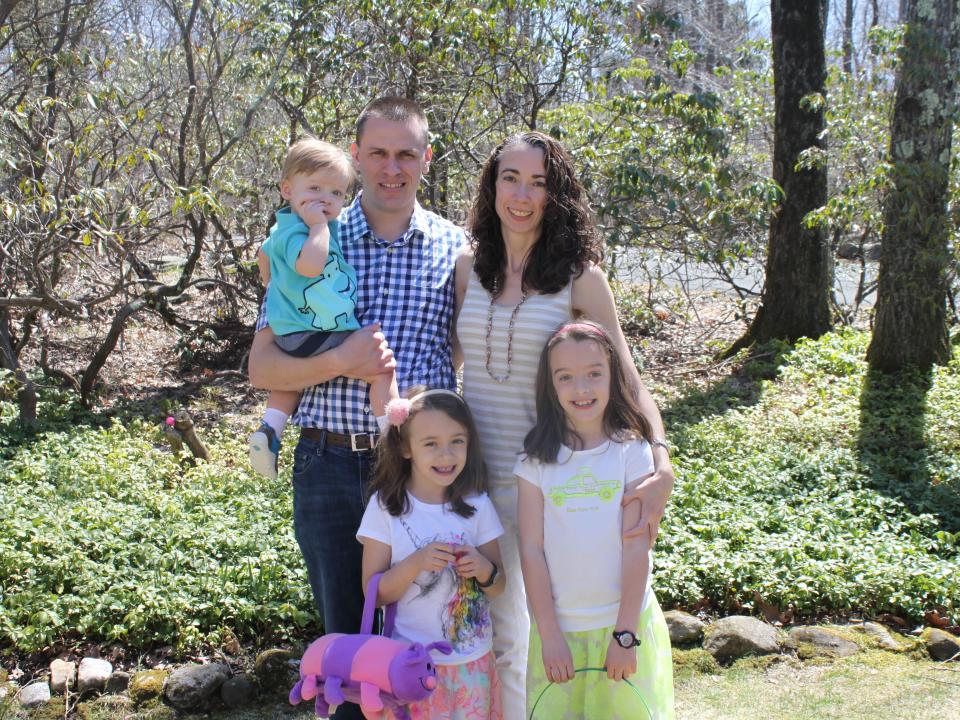 The Seitz family pose for a portrait on a patch of grass in front of a cluster of trees.