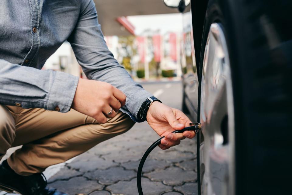 close up of man crouching on the gas station and inflating tire