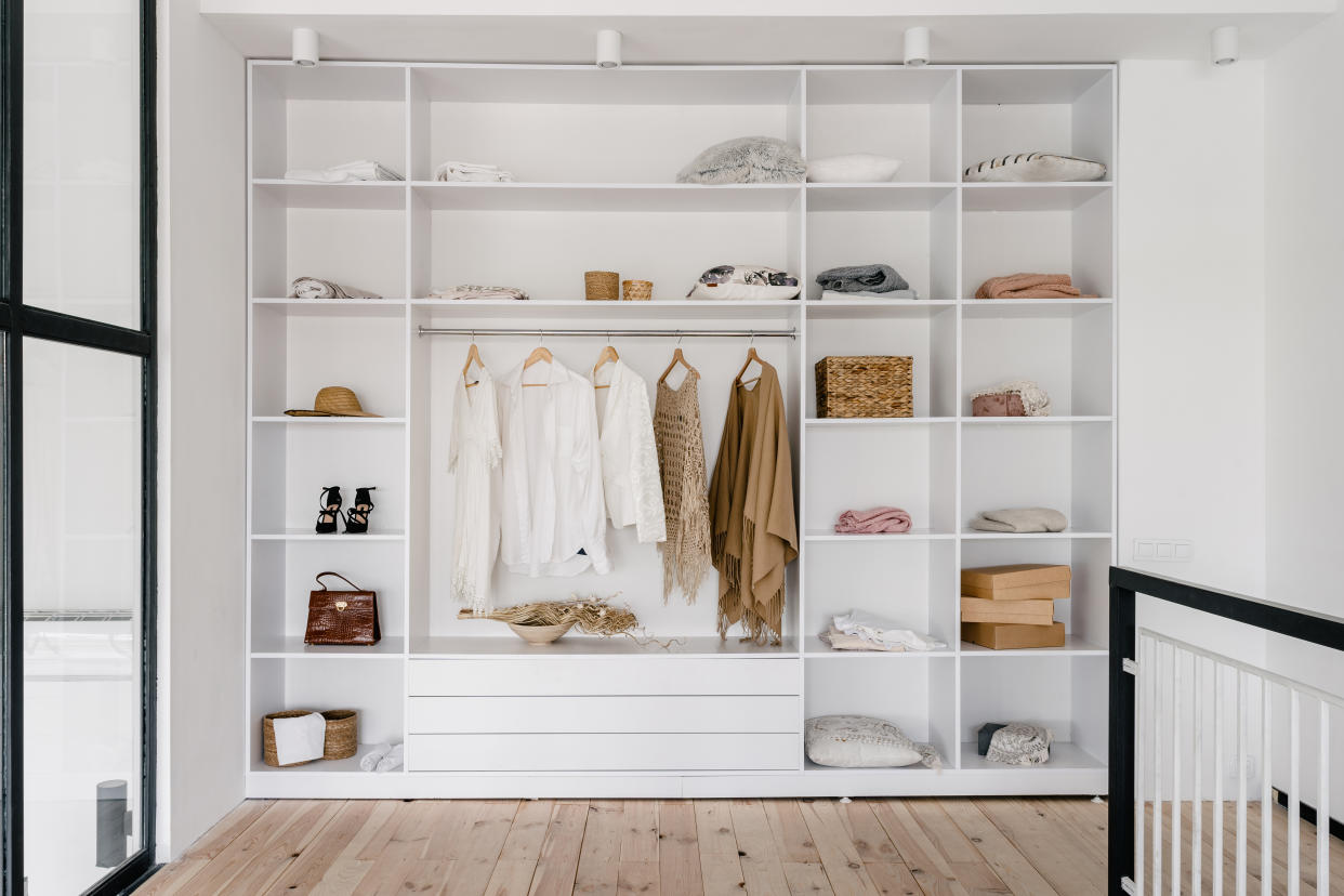  An open closet with white shelves and organized clothes . 