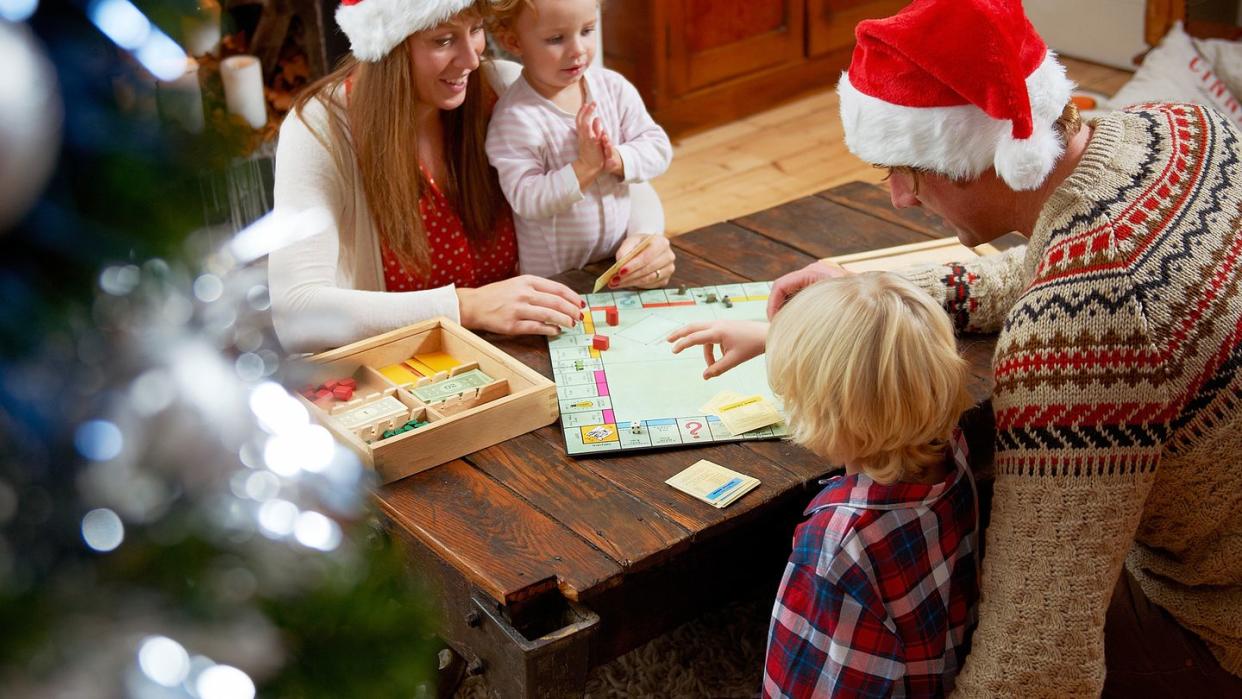 family playing board game around table, parents in christmas hats