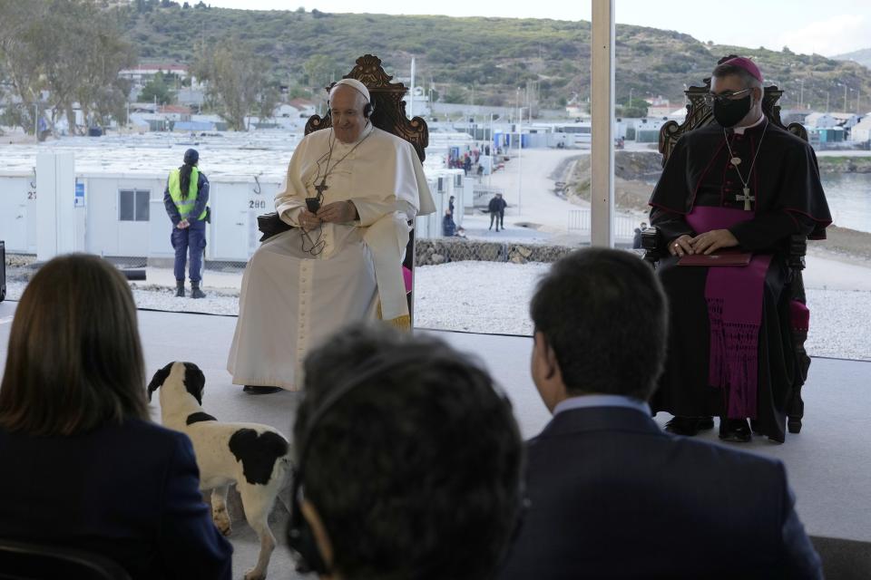 Pope Francis smiles as a stray dog stands in front of him during a ceremony at the Karatepe refugee camp, on the northeastern Aegean island of Lesbos, Greece, Sunday, Dec. 5, 2021. Pope Francis is returning to Lesbos, the Greek island that was at the heart of a massive wave of migration into Europe. (AP Photo/Alessandra Tarantino)