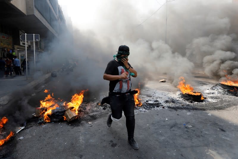 An Iraqi demonstrator jump above burning tires as he blocks the road during ongoing anti-government protests, in Baghdad