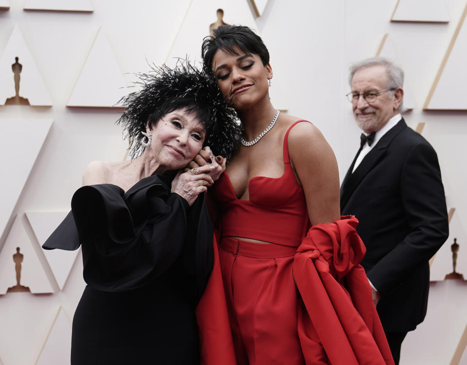 Rita Moreno, izquierda, y Ariana DeBose llegan a los Oscar el 27 de marzo de 2022 en el Teatro Dolby en Los Angeles. Al fondo mira Steven Spielberg. (Foto AP/Jae C. Hong)