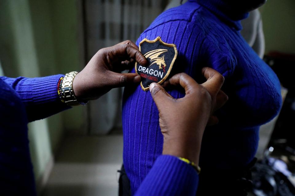 A member of the female-only security team Dragon Squad Limited, assists Peace Vigorous puts on her badge (Reuters)