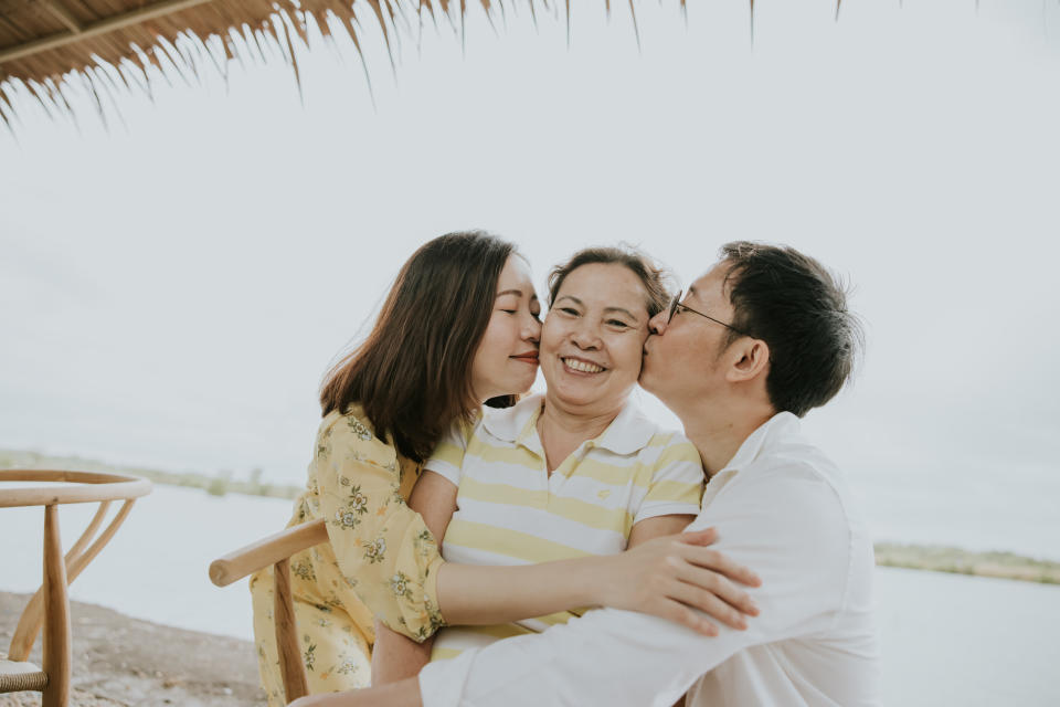 Photo of Asian family, son and daughter kissing their mom while on their holidays trip at the beach with their active mom.