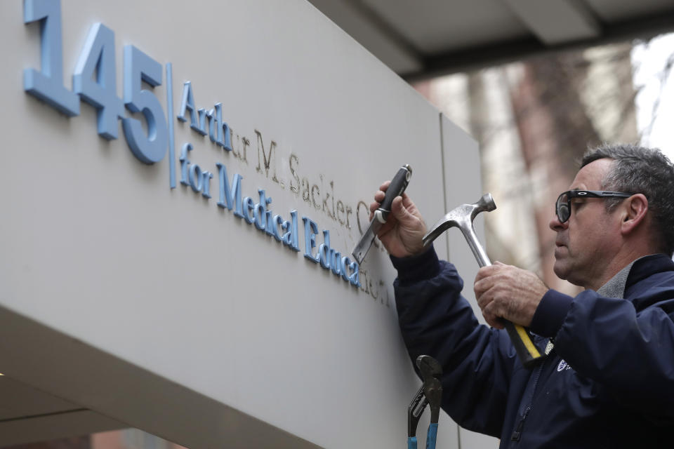 Worker Gabe Ryan removes a sign that includes the name Arthur M. Sackler at an entrance to Tufts School of Medicine, Thursday, Dec. 5, 2019, in Boston. Tufts University says it is stripping the Sackler name from its campus in recognition of the family's connection to the opioid crisis. (AP Photo/Steven Senne)