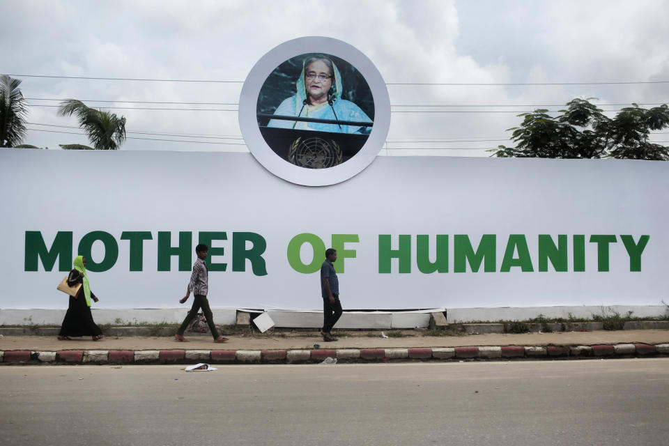 FILE- Bangladeshis walk past a banner lauding Prime Minister Sheikh Hasina as the 'Mother of Humanity,' for her continuous support to nearly 1 million Rohingya Muslims who fled neighboring Myanmar to escape violence, in Dhaka, Bangladesh, Oct. 7, 2017. The elections in Bangladesh are all about one person: Prime Minister Sheikh Hasina. Analysts predict that since the main opposition party is staying out of the Jan. 7 vote, the 76-year-old leader is practically guaranteed her fifth term in office. (AP Photo/A.M. Ahad, File)