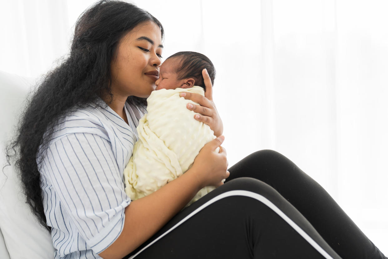 Happy mother carrying and kissing on newborn baby on bed. Young mom or nurse taking care newborn in the hospital